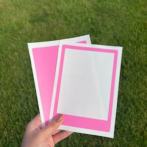 May include: Two pink photo frame stickers with white borders. The stickers are blank and ready to be decorated.