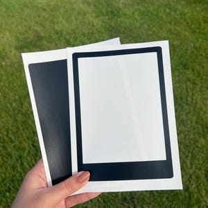 May include: Two black framed photo stickers with white backgrounds. The stickers are on a white surface.