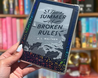 Puede incluir: Un lector electrónico negro con una funda protectora transparente que presenta un borde de purpurina holográfica multicolor. La pantalla muestra la portada del libro The Summer of Broken Rules de K. L. Walther con un velero ilustrado.