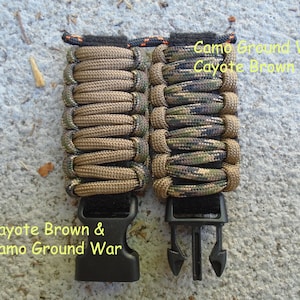 May include: Two paracord bracelets with black buckles. The bracelet on the left is brown and the bracelet on the right is camouflage with green, brown, and black colors. The text "Coyote Brown & Camo Ground War" is written below the bracelets.