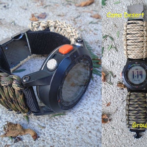 May include: Two black Garmin watches with different camouflage paracord straps. The watch on the left has a green, brown, and black strap labeled "Ground War". The watch on the right has a tan and black strap labeled "Camo Desert".