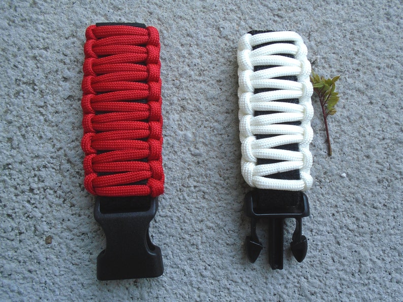 May include: Two paracord bracelets with black buckles. One bracelet is red and the other is white.