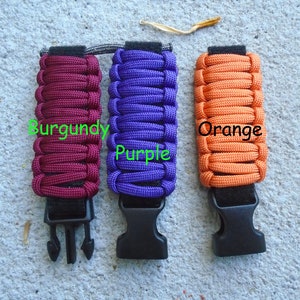 May include: Three paracord bracelets with black buckles. The bracelets are burgundy, purple, and orange.
