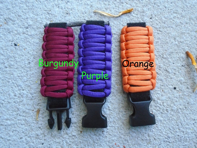 May include: Three paracord bracelets with black buckles. The bracelets are burgundy, purple, and orange.