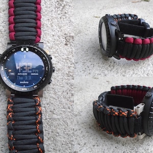 May include: A black Suunto watch with a red and black paracord strap. The watch face displays the time, date, and altitude.