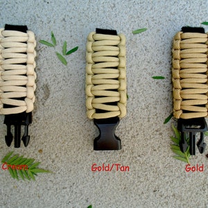 May include: Three paracord bracelets in cream, gold/tan, and gold colours. Each bracelet has a black plastic buckle.