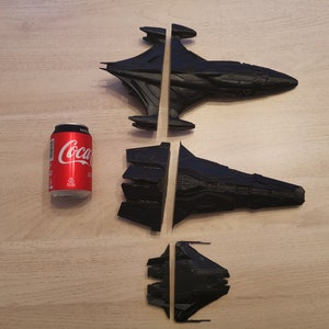 Puede incluir: Tres naves espaciales de pl&aacute;stico negro, dos de las cuales est&aacute;n divididas por la mitad, est&aacute;n dispuestas sobre una superficie de madera. Una lata de Coca-Cola est&aacute; en el fondo para la escala.