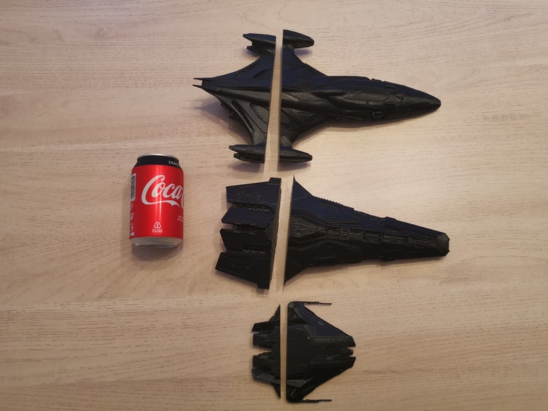 Puede incluir: Tres naves espaciales de pl&aacute;stico negro, dos de las cuales est&aacute;n divididas por la mitad, est&aacute;n dispuestas sobre una superficie de madera. Una lata de Coca-Cola est&aacute; en el fondo para la escala.