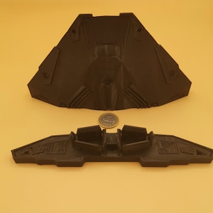 Puede incluir: Un modelo de nave espacial impreso en 3D de color negro con dos partes. La parte superior es de forma triangular con una nariz puntiaguda y la parte inferior es una forma de ala plana con tres vainas de motor.