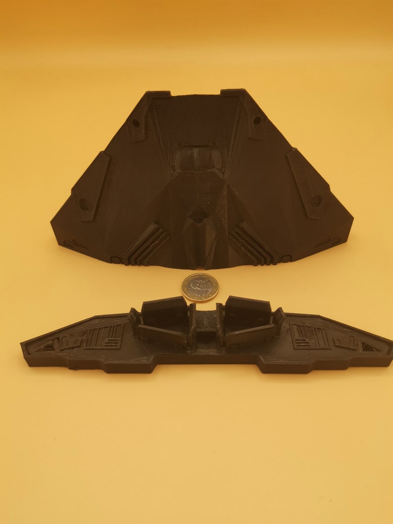 Puede incluir: Un modelo de nave espacial impreso en 3D de color negro con dos partes. La parte superior es de forma triangular con una nariz puntiaguda y la parte inferior es una forma de ala plana con tres vainas de motor.