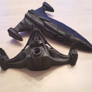 Puede incluir: Dos modelos de naves espaciales impresos en 3D de color negro. El modelo m&aacute;s grande es una nave larga y elegante con una nariz puntiaguda. El modelo m&aacute;s peque&ntilde;o es una nave m&aacute;s compacta, triangular, con tres motores.