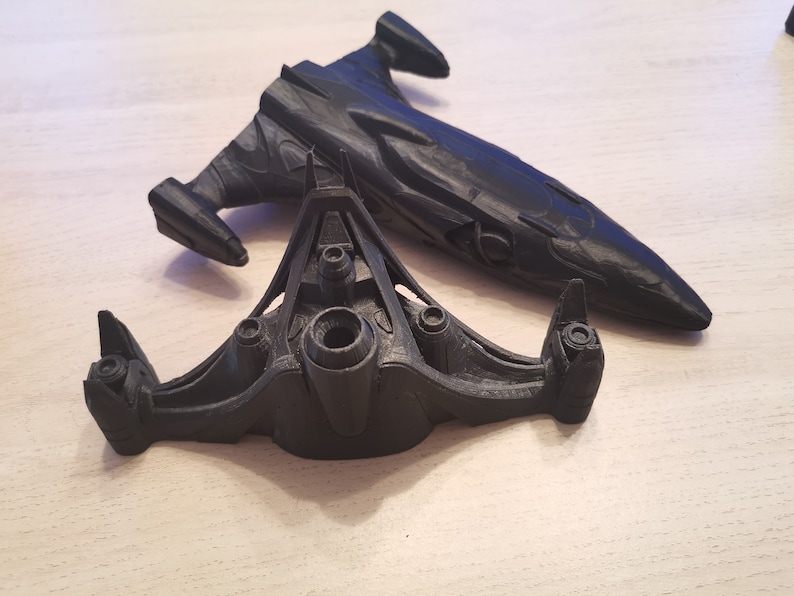 Puede incluir: Dos modelos de naves espaciales impresos en 3D de color negro. El modelo m&aacute;s grande es una nave larga y elegante con una nariz puntiaguda. El modelo m&aacute;s peque&ntilde;o es una nave m&aacute;s compacta, triangular, con tres motores.