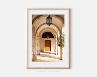 May include: A framed vertical photograph of a stone archway corridor featuring light-colored masonry, a wooden door at the end, and hanging lanterns. The image includes the text "photographed with love by jamie brogdon" at the bottom.