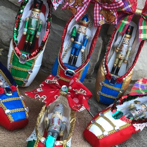 May include: Six decorated ballet shoes with nutcracker figurines inside. Each shoe has a different color scheme and bow. The shoes are decorated with rhinestones, sequins, and lace.