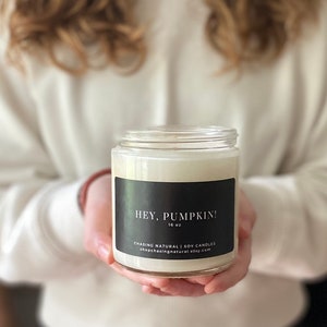 May include: A white soy candle in a clear glass jar with a black label that reads "Hey, Pumpkin!" 16 oz. CHASING NATURAL | SOY CANDLES shopchasingnatural.etsy.com