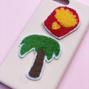 May include: A pink phone case with a green palm tree and a red and yellow french fry design. The case has the letters "S|B" printed on the bottom.