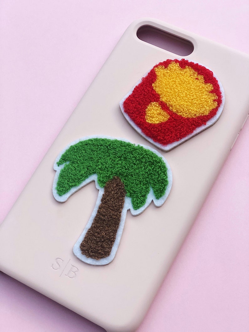May include: A pink phone case with a green palm tree and a red and yellow french fry design. The case has the letters "S|B" printed on the bottom.