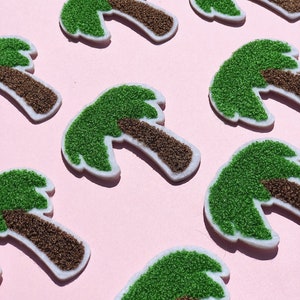 Puede incluir: Ocho parches de palmeras de fieltro verde y marrón sobre un fondo rosa. Las palmeras son todas del mismo tamaño y forma, y están dispuestas en un patrón escalonado.