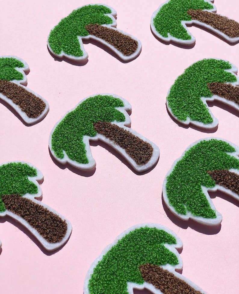 May include: Eight green and brown felt palm tree patches on a pink background. The palm trees are all the same size and shape, and they are arranged in a staggered pattern.