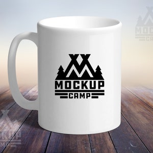 May include: White ceramic mug with a black logo that says "MOCKUP CAMP" with a graphic of two mountains and trees.