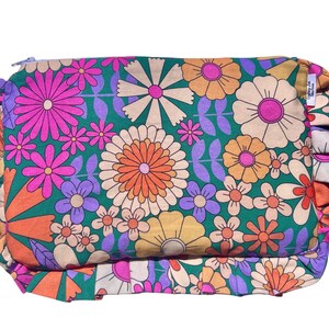 May include: A green fabric pouch with a floral print featuring pink, orange, and yellow flowers. The pouch has a ruffled edge and a zipper closure. The text "Enjoy Life" is printed on the pouch.
