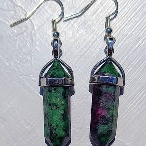May include: A pair of silver earrings with green and pink gemstone pendants. The pendants are shaped like long, pointed crystals.
