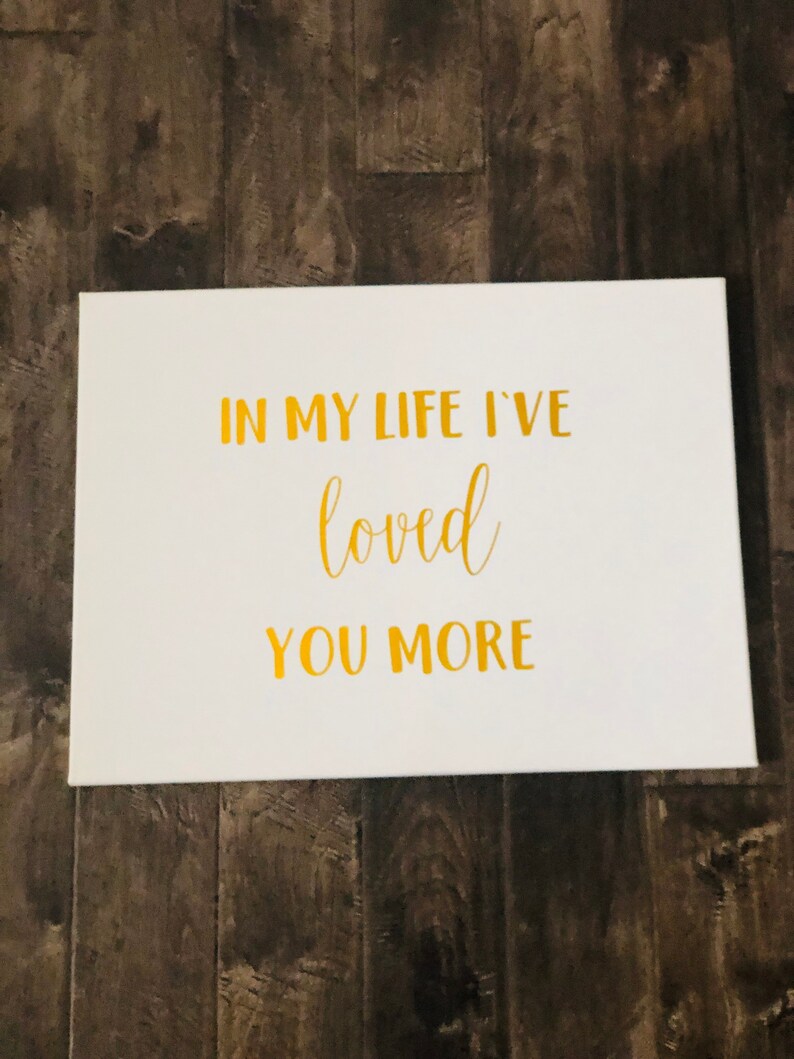 May include: White canvas with gold lettering that reads "In my life I've loved you more".