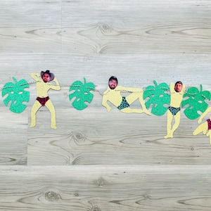 May include: A yellow and green paper banner with cutouts of people wearing swimsuits and tropical leaves. Each cutout has a different person's face in it.