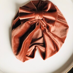 Puede incluir: Un turbante de terciopelo rosa polvoriento con un gran lazo en la parte superior.