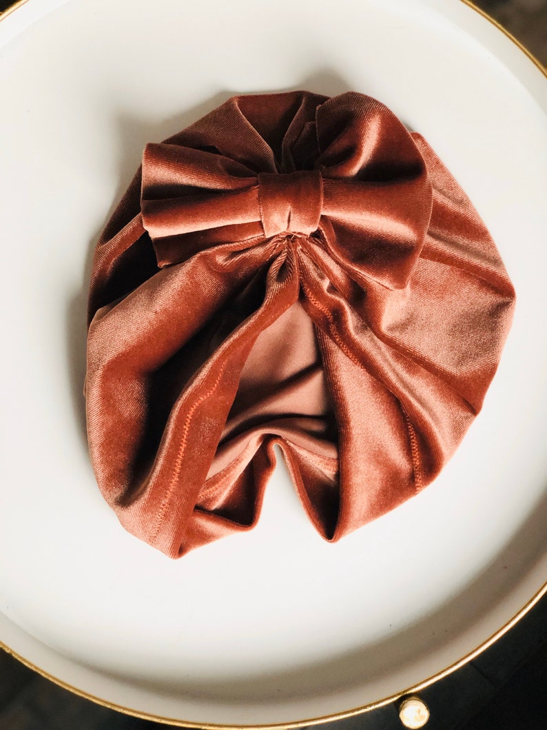 Puede incluir: Un turbante de terciopelo rosa polvoriento con un gran lazo en la parte superior.