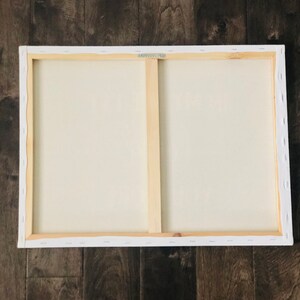 May include: The back of a stretched canvas painting with a wooden frame. The canvas is white and the frame is natural wood.