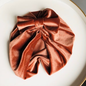 Puede incluir: Un turbante de terciopelo color &oacute;xido con un gran lazo en la parte superior.