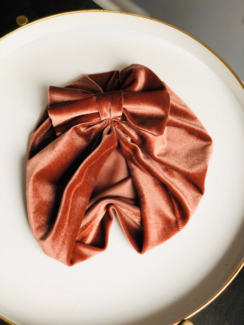 Puede incluir: Un turbante de terciopelo color &oacute;xido con un gran lazo en la parte superior.