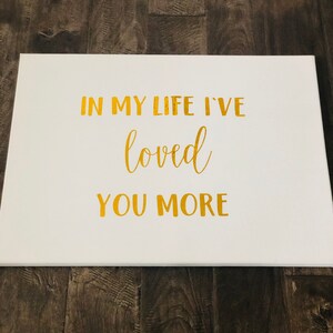 May include: White canvas with gold lettering that reads "In my life I've loved you more".