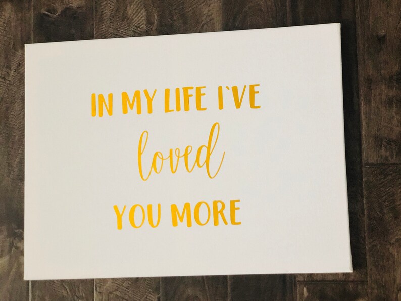 May include: White canvas with gold lettering that reads "In my life I've loved you more".