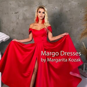 May include: A woman wearing a red off-the-shoulder gown with a thigh-high slit. The gown has a sweetheart neckline and a flowing skirt. The text "Margo Dresses by Margarita Kozak" is visible in the image.