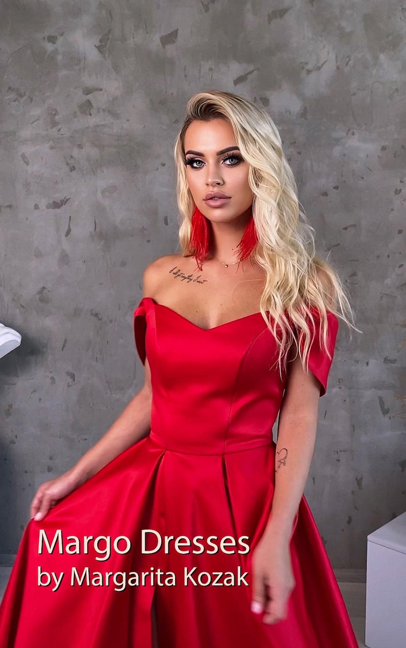 May include: A woman wearing a red off-the-shoulder gown with a sweetheart neckline. The gown has a flowing skirt and is made of a satin-like fabric. The text "Margo Dresses by Margarita Kozak" is visible at the bottom of the image.