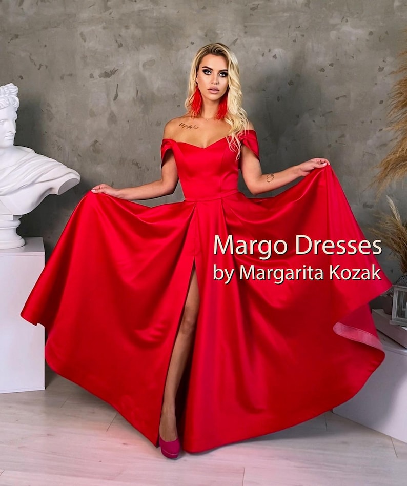 May include: A woman wearing a red off-the-shoulder gown with a thigh-high slit. The gown has a sweetheart neckline and a flowing skirt. The text "Margo Dresses by Margarita Kozak" is visible in the image.