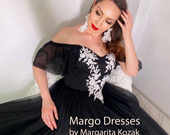 Puede incluir: Vestido negro con hombros descubiertos, falda amplia y bordado floral blanco en el corpiño. El vestido es de Margo Dresses by Margarita Kozak. La modelo lleva pendientes blancos grandes y pintalabios rojo.