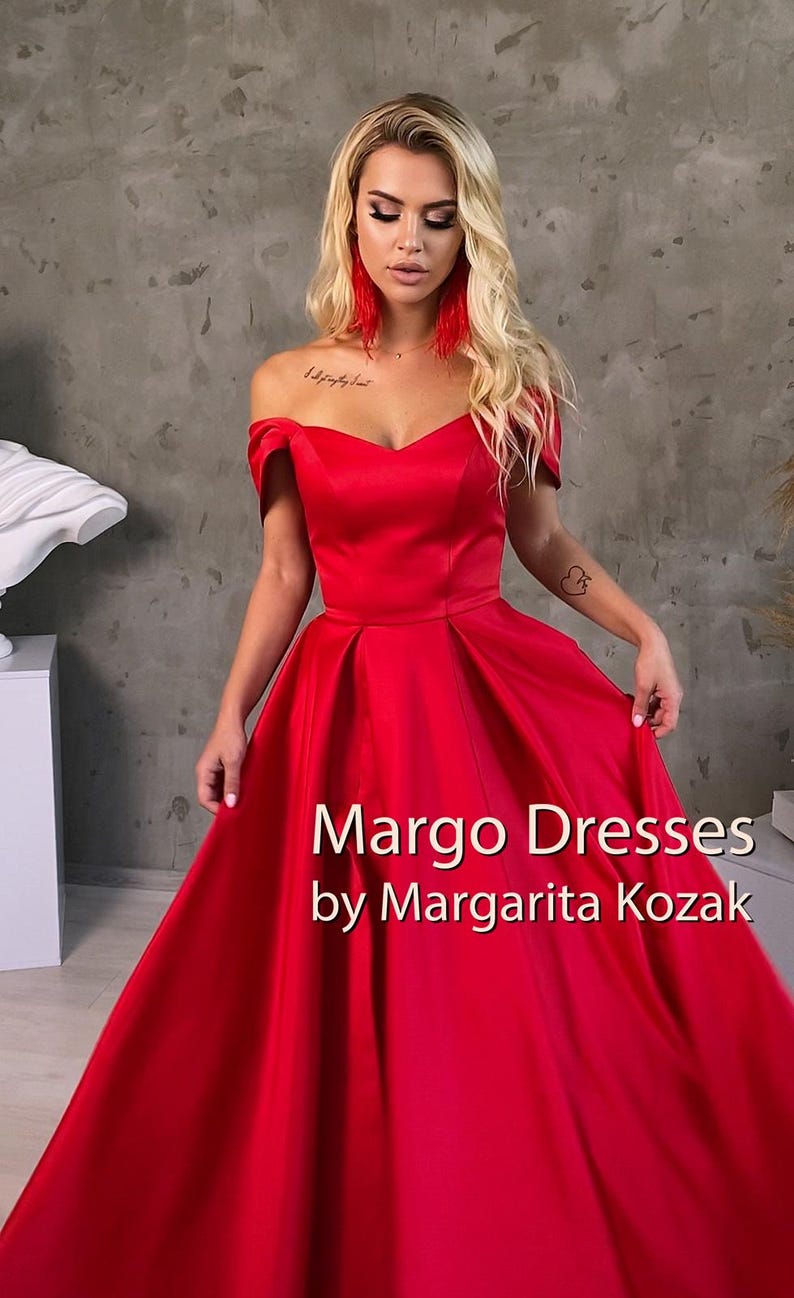 May include: A woman wearing a red off-the-shoulder gown with a sweetheart neckline. The gown has a full skirt and is made of a satin fabric. The text "Margo Dresses by Margarita Kozak" is displayed at the bottom of the image.