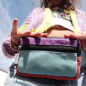 Puede incluir: Una riñonera de tela multicolor con una cremallera negra y una etiqueta blanca que dice "ASACQUA2".