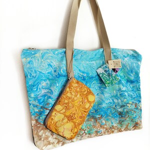 Puede incluir: Un bolso tote grande y una pequeña bolsa a juego. El bolso presenta un diseño veteado azul y blanco, que recuerda a las olas del océano, con asas beige y cremallera. La bolsa pequeña tiene un patrón veteado amarillo y marrón.