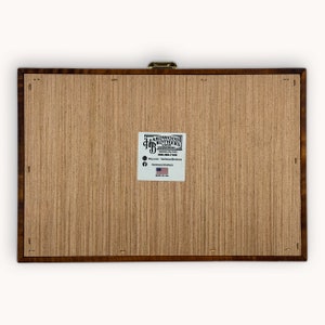 May include: A wooden box with a brass latch. The box is made by Hardwood Brothers Custom Woodworking in Waverly, Ohio. The box has a label with the company's name, website, and phone number. The label also includes a small American flag and the words "Made in USA".