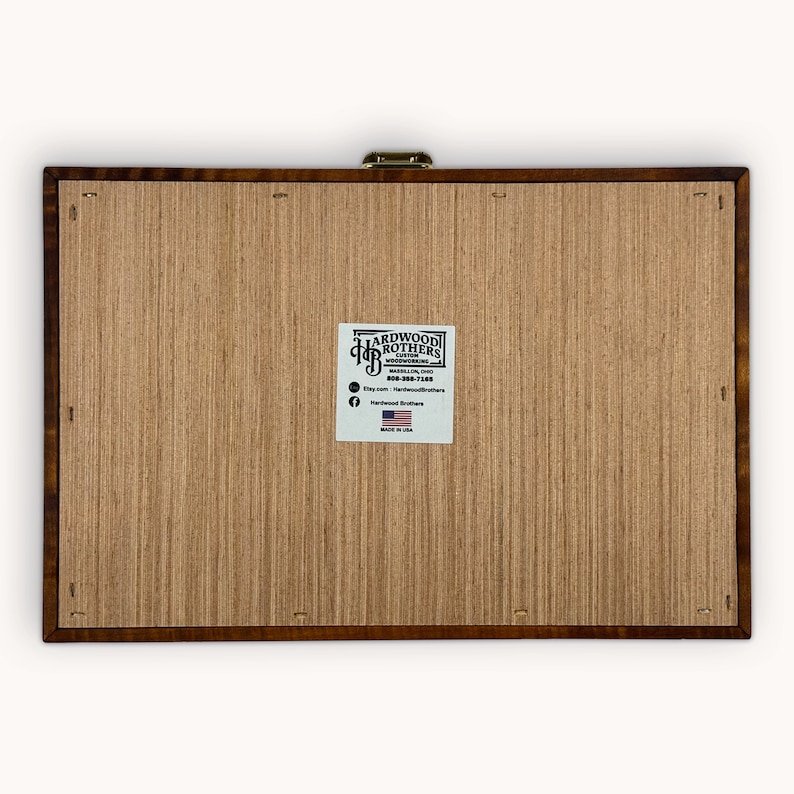 May include: A wooden box with a brass latch. The box is made by Hardwood Brothers Custom Woodworking in Waverly, Ohio. The box has a label with the company's name, website, and phone number. The label also includes a small American flag and the words "Made in USA".