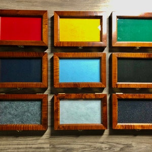 May include: Nine wooden display boxes with different colored felt inserts. The boxes are arranged in three rows of three. The boxes are made of wood with a natural finish. The felt inserts are red, yellow, green, blue, black, gray, light blue, dark gray, and black.