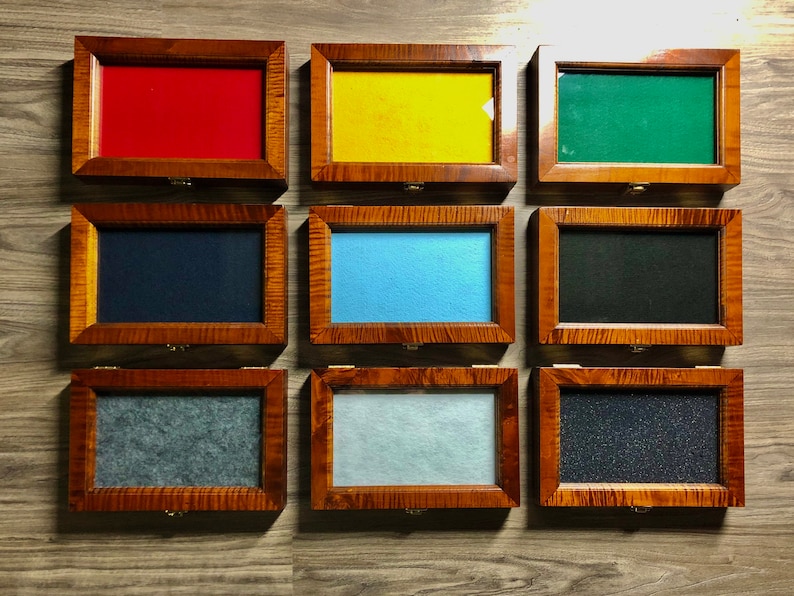 May include: Nine wooden display boxes with different colored felt inserts. The boxes are arranged in three rows of three. The boxes are made of wood with a natural finish. The felt inserts are red, yellow, green, blue, black, gray, light blue, dark gray, and black.