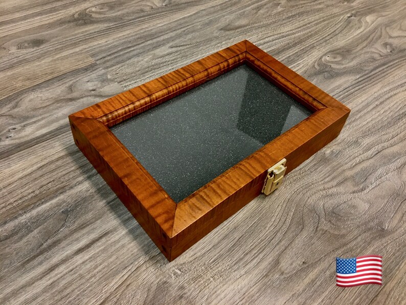 May include: A wooden display case with a glass top and a brass latch. The case is made of light brown wood with a dark brown stain. The case is sitting on a wood floor.
