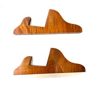 Op de afbeelding: Twee houten displaystandaards met een gebogen vorm en een uitsparing in het midden. De standaards zijn gemaakt van lichtbruin hout met een roodachtige tint.