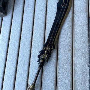 Può includere: Una spada nera e dorata con dettagli intricati, che giace su una superficie di legno innevata.