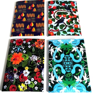 Puede incluir: Cuatro cuadernos con cubiertas coloridas. Uno tiene un fondo azul marino con formas amarillas y naranjas. Otro presenta un pájaro posado en una rama con frutos rojos. Un tercero tiene un diseño floral con mariposas. El último tiene un patrón azul y verde.